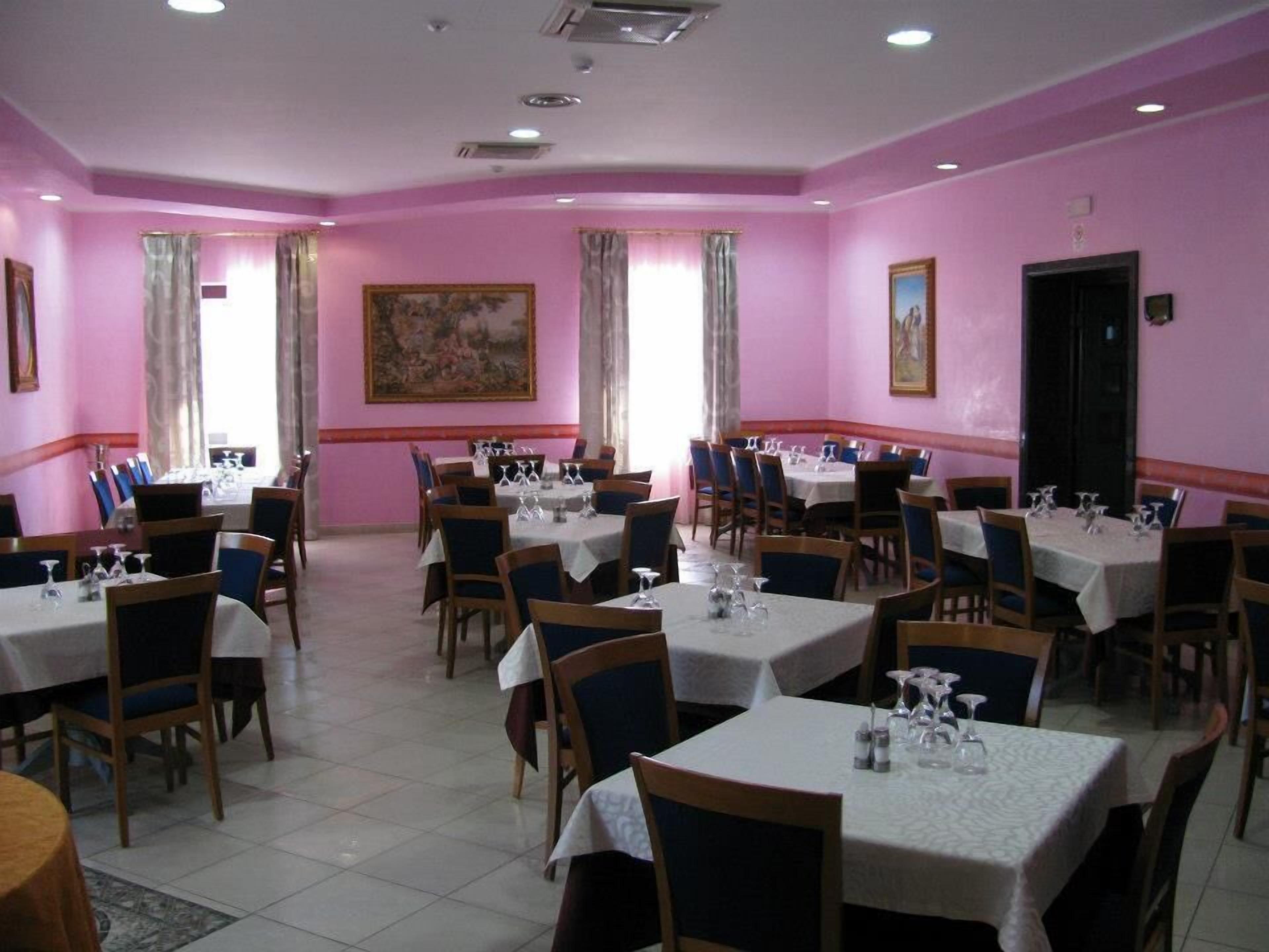 Un'area pranzo con pareti rosa, diversi tavoli con sedie e quadri alle pareti.