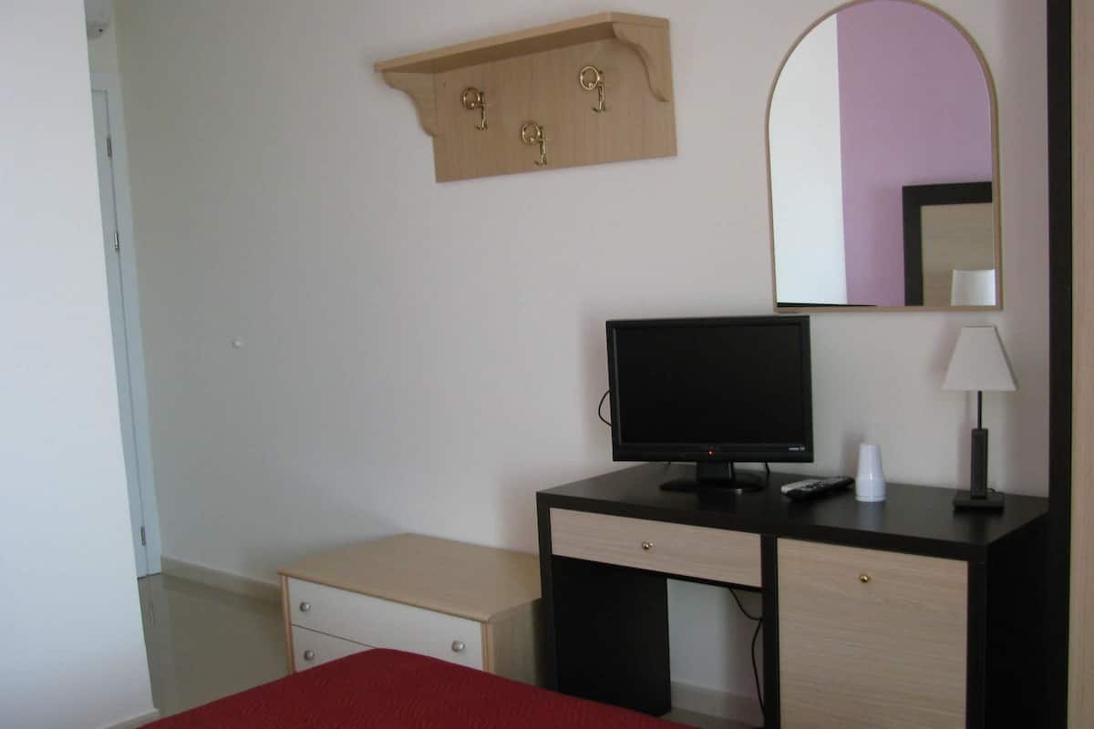 Habitación de hotel con cama, escritorio con computadora, espejo y un pequeño estante con llaves.