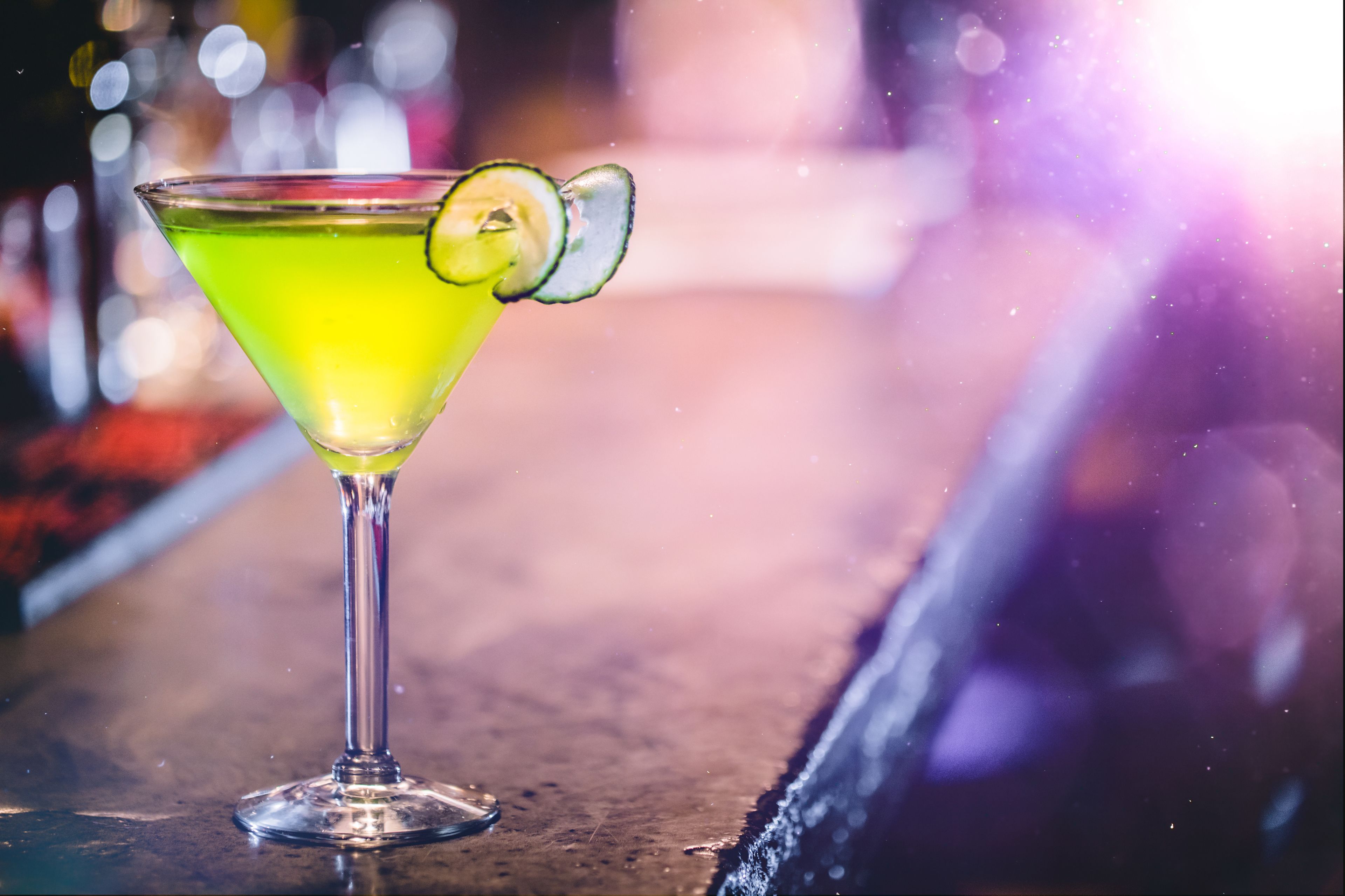 A cocktail in a martini glass with a lime garnish on a bar counter.