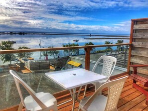 A balcony with a table and chairs, overlooking a calm body of water and distant shoreline. - Auberg'Inn - Aux 4 Vents (Carleton-sur-Mer)