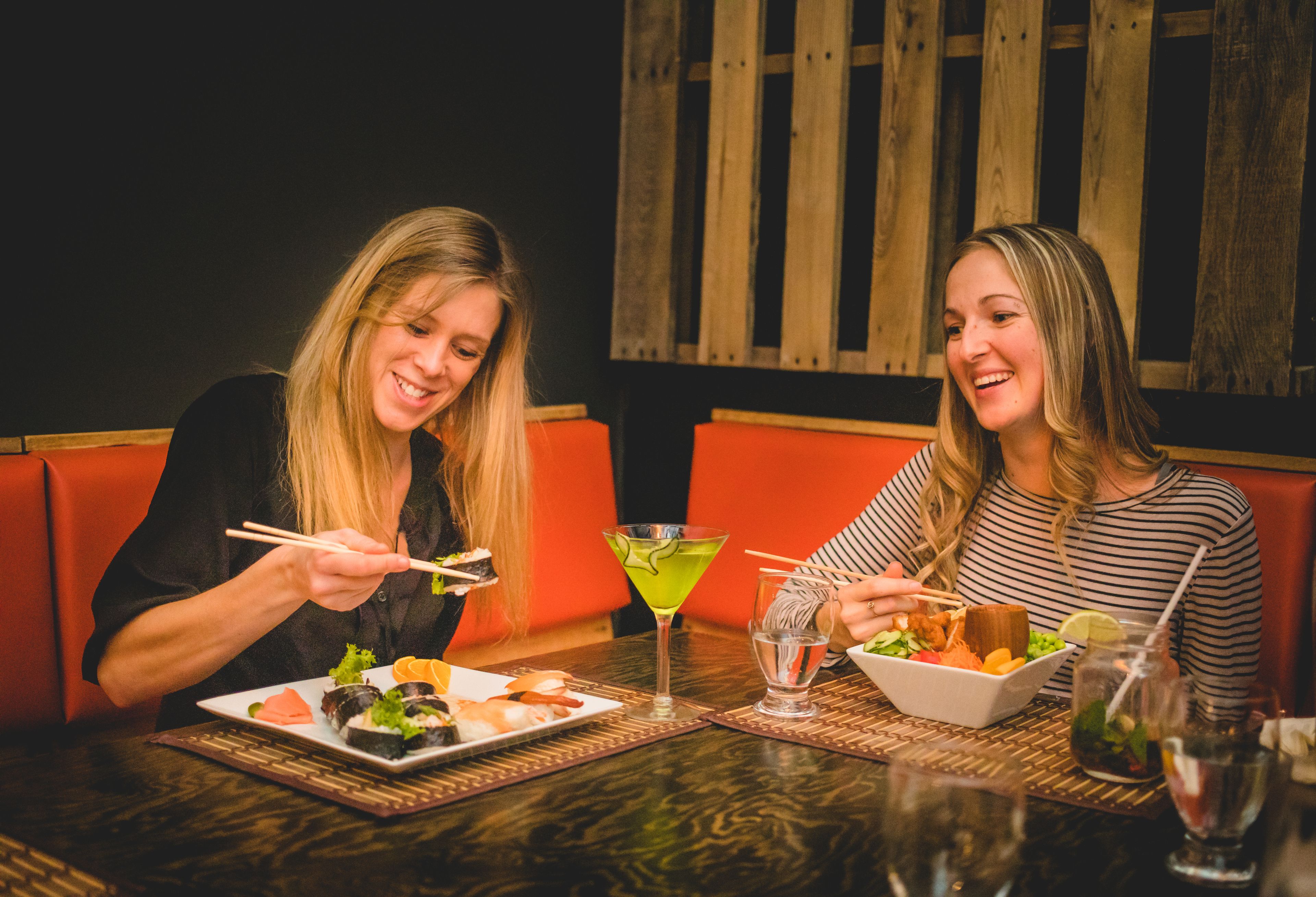 Dos personas cenando en un restaurante, con sushi y cócteles sobre la mesa.