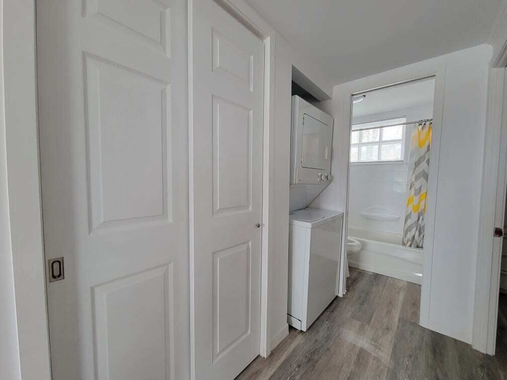 Un pasillo con puertas blancas, zona de lavandería y ducha con toalla amarilla.