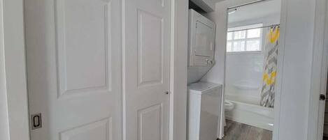 Un pasillo con puertas blancas, zona de lavandería y ducha con toalla amarilla.