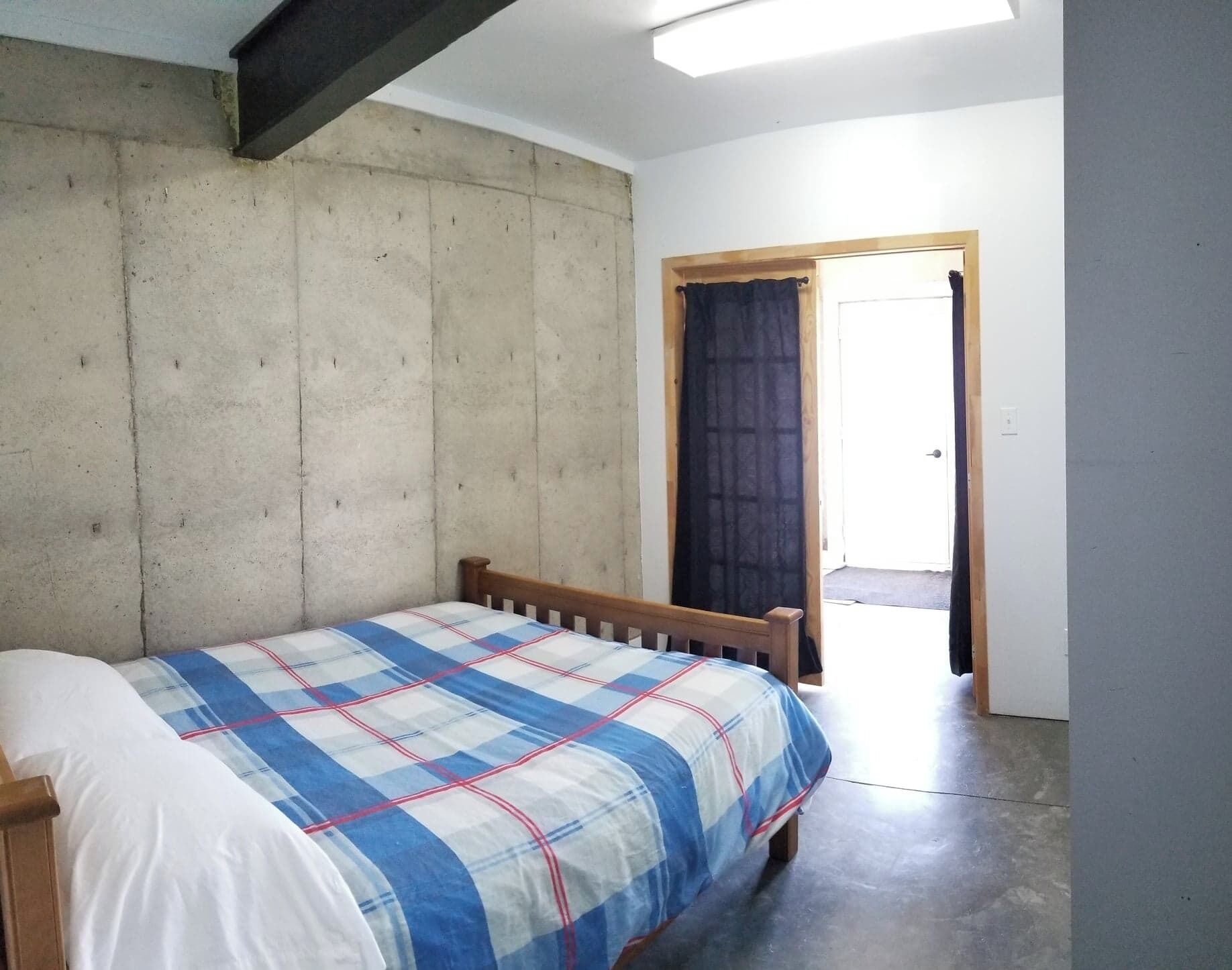 A bedroom with a bed, a concrete wall, a wooden door, and a skylight.