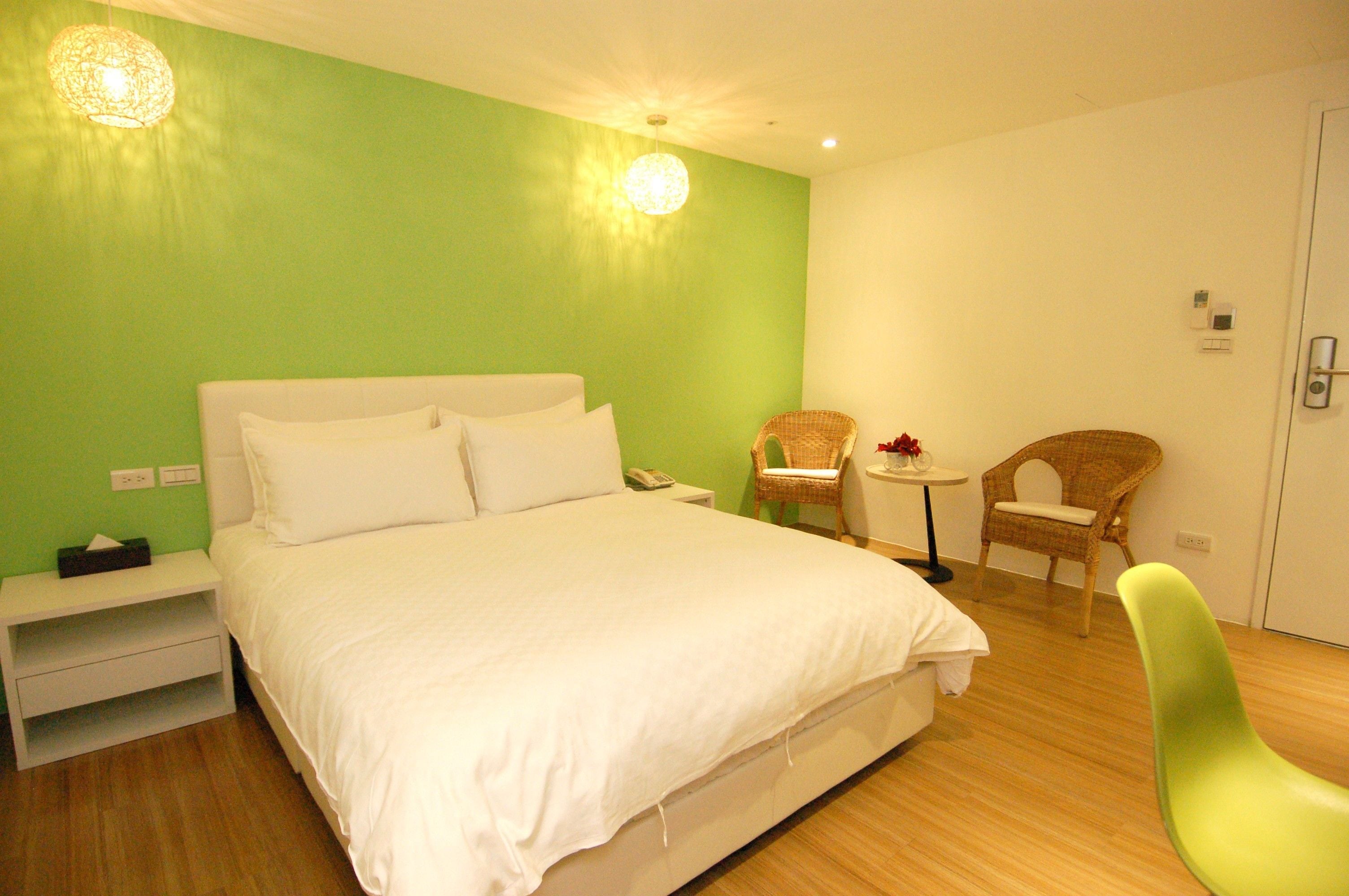 Una habitación de hotel con una cama grande, una mesita con una silla y un sillón verde.