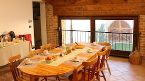 Een houten eettafel met stoelen, een buffet met eten en drinken, en uitzicht op een schuur door een glazen deur.