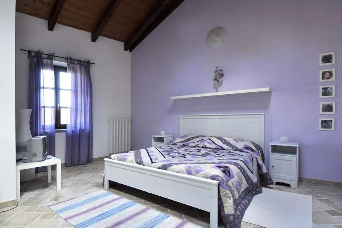 Ein Schlafzimmer mit Bett, Schreibtisch, Heizkörper und einem Fenster mit Vorhängen.