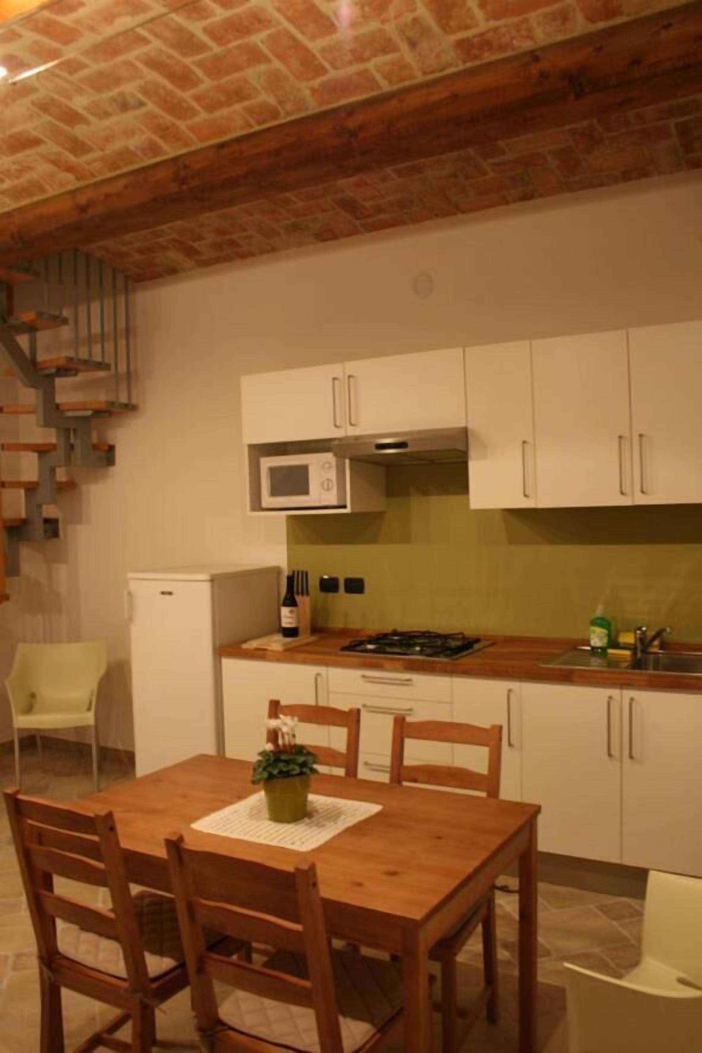 Una cocina compacta con armarios blancos, microondas, refrigerador pequeño y una mesa de comedor de madera con sillas.