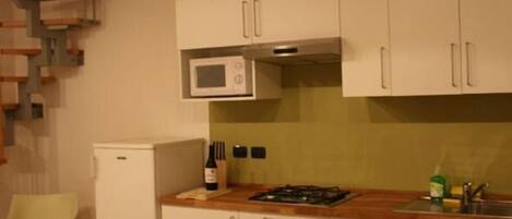 Una cocina compacta con armarios blancos, microondas, refrigerador pequeño y una mesa de comedor de madera con sillas.