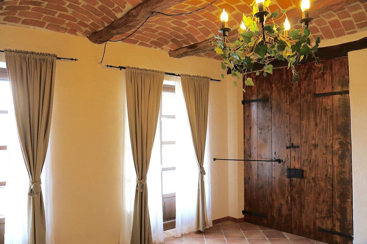 Ein Zimmer mit Ziegeldecke, Holztür und Vorhängen an den Fenstern.