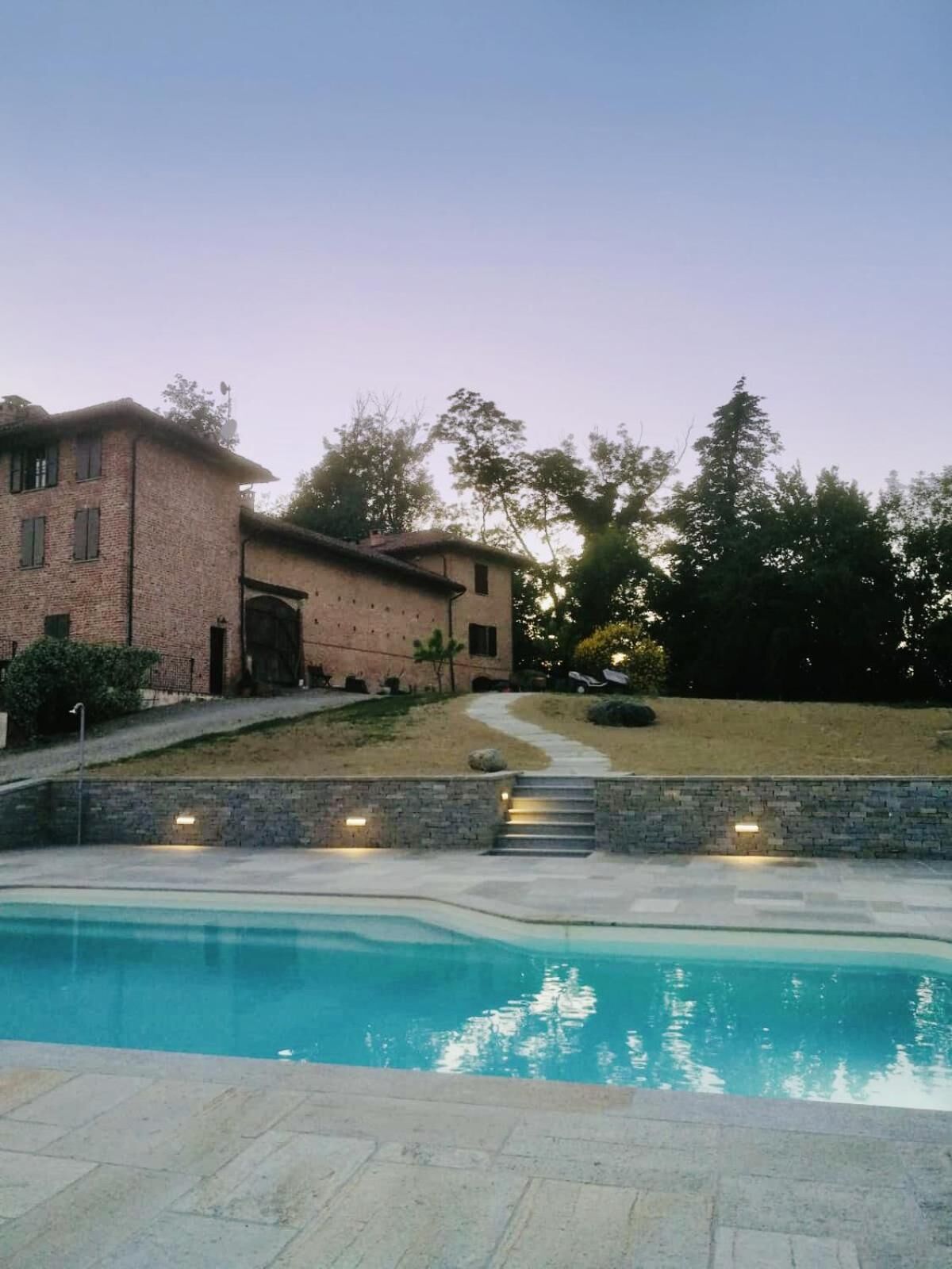 Una casa de ladrillo con piscina, un sendero de piedra y una colina cubierta de césped.