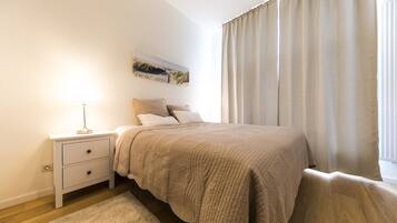 A bedroom with a bed, a nightstand, a lamp, a painting on the wall, and a window with curtains.