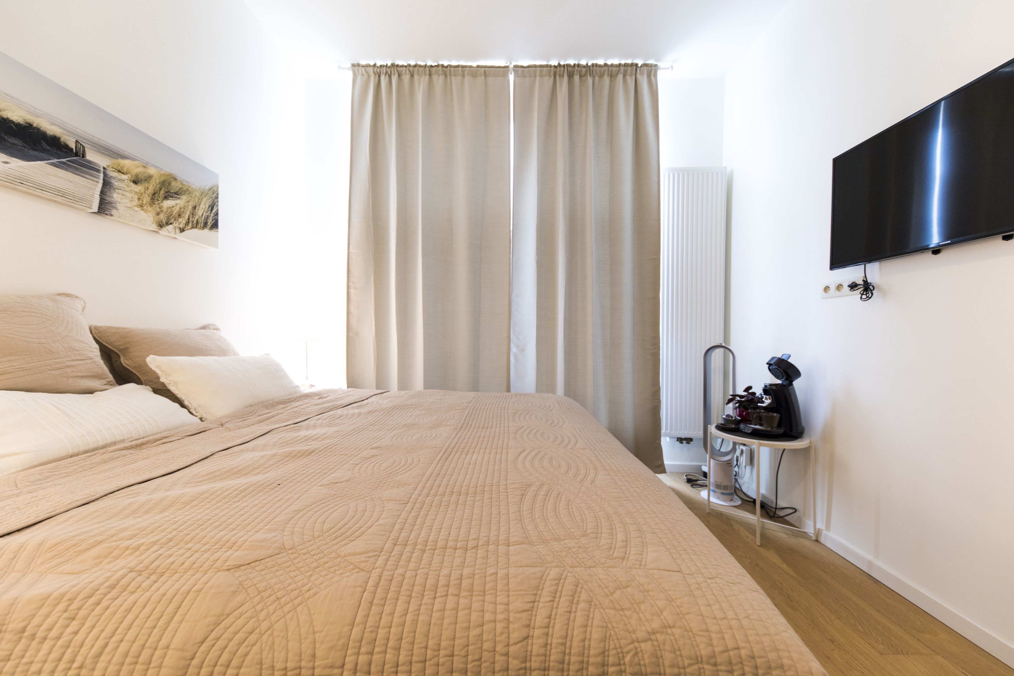 Een slaapkamer met een groot bed, een flatscreen televisie aan de muur, een radiator en een koffieapparaat op een klein tafeltje.