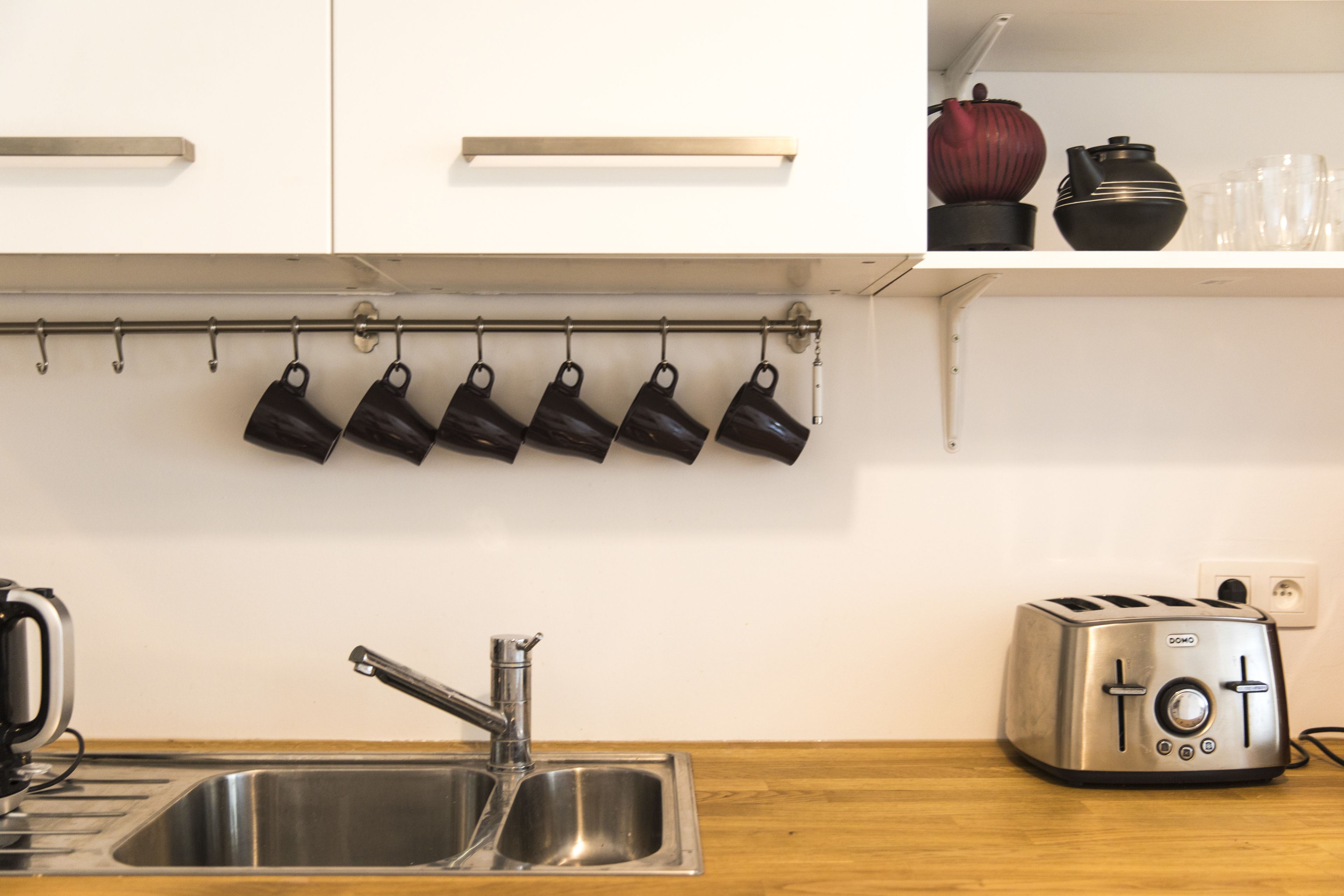 A kitchen with a stainless steel sink, a toaster, and a row of hanging black mugs.
