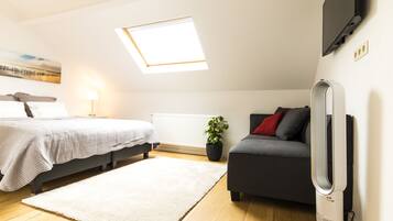 A modern bedroom with a bed, a sofa, a TV, and a skylight.