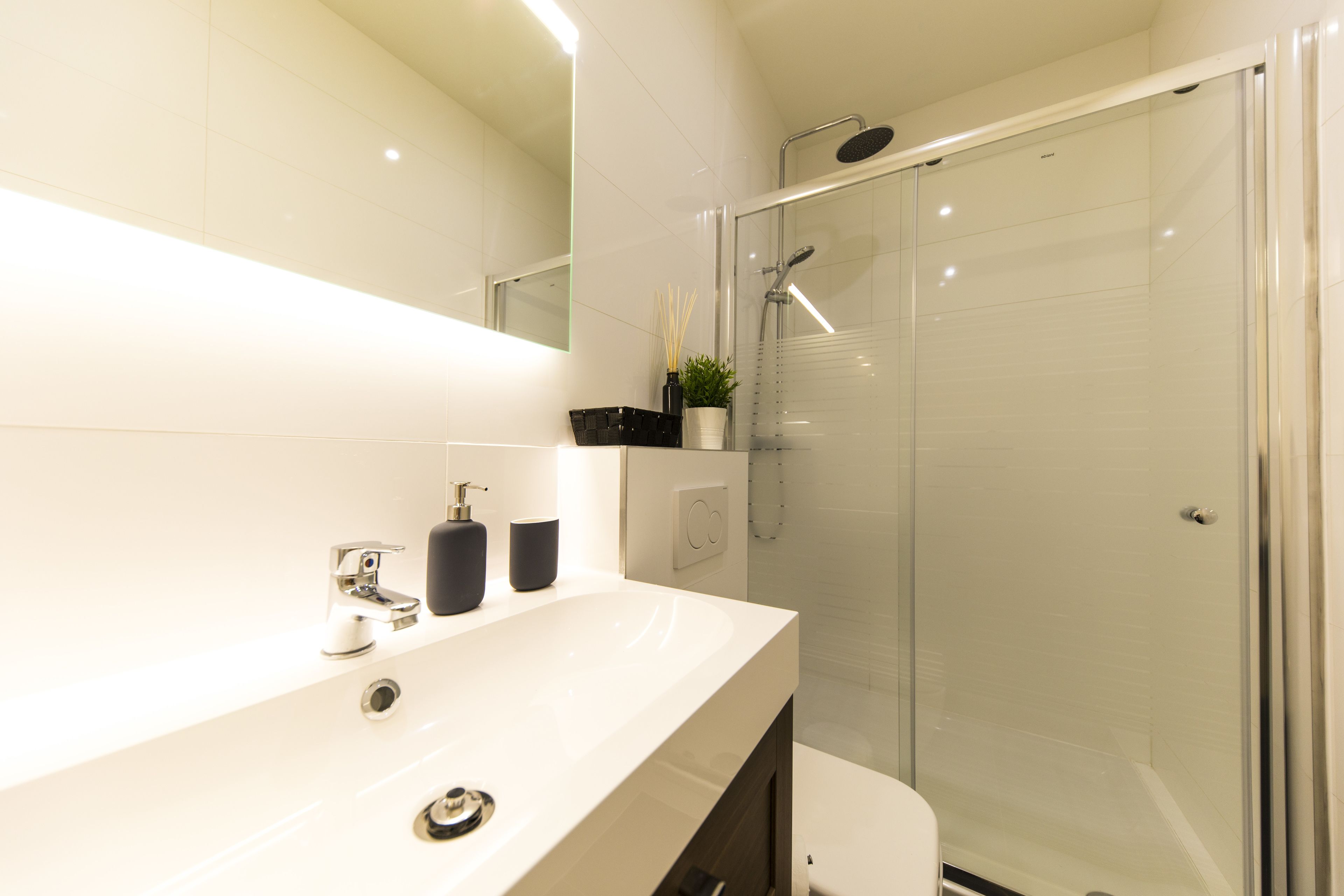 A modern bathroom with a white sink, a glass shower enclosure, and a large mirror.