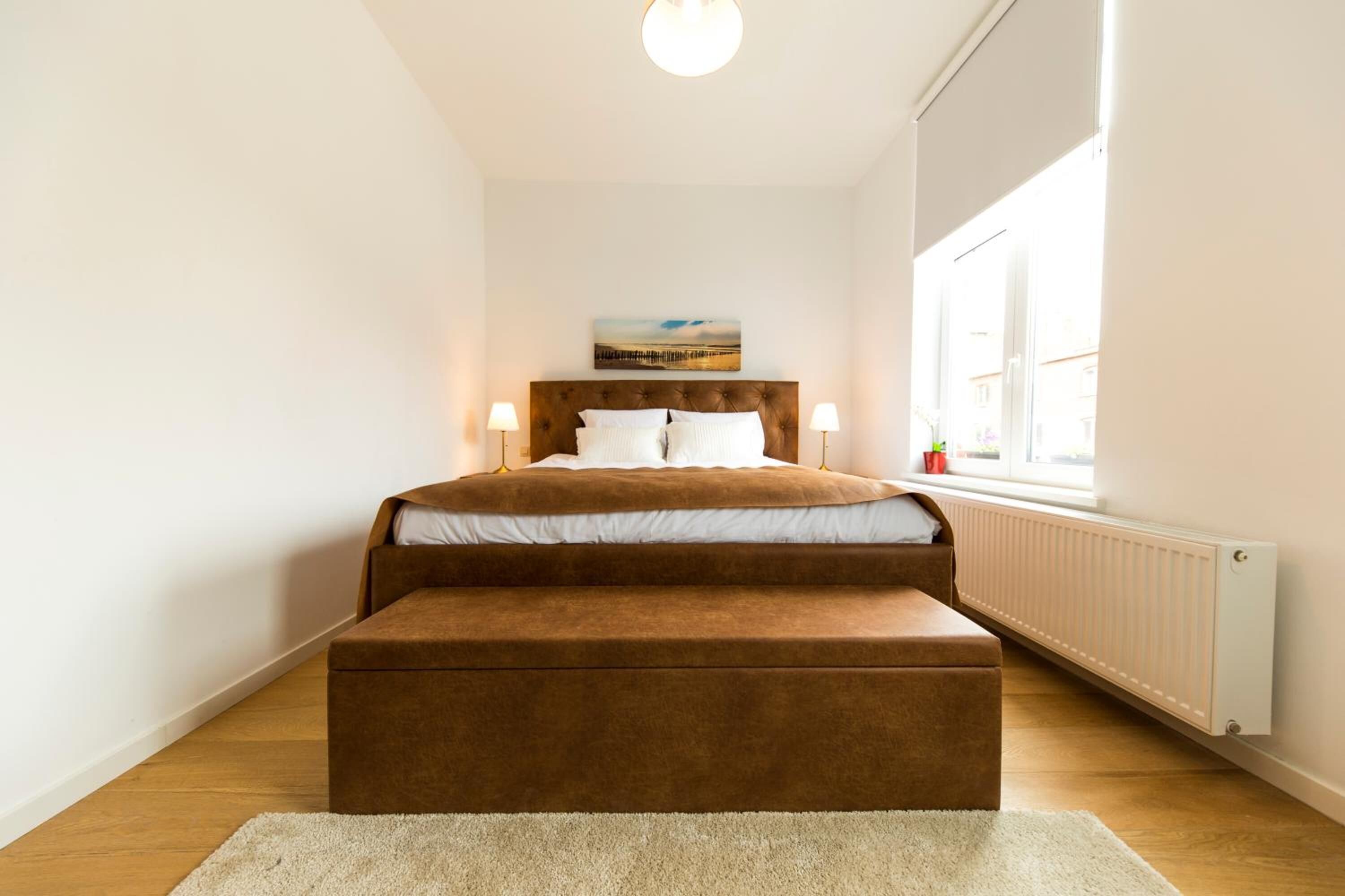 Une chambre à coucher avec un lit, une fenêtre, un radiateur et un tableau accroché au mur.