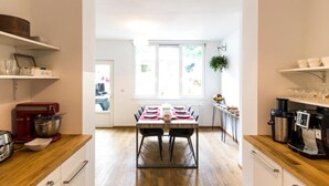A modern kitchen with wooden flooring, white cabinets, and a dining area with a table set for four. - B&B Daya (Leuven)