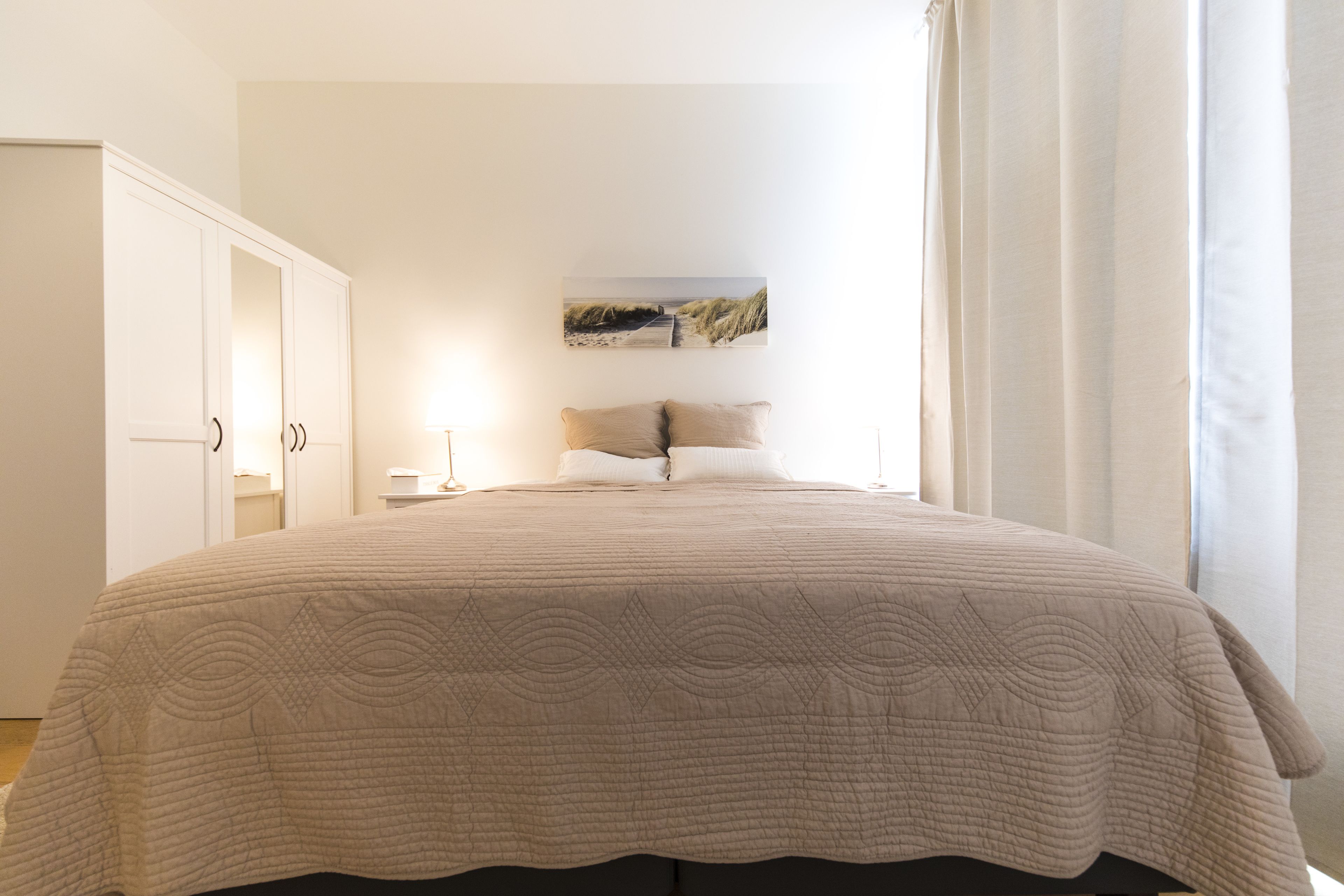 A bedroom with a large bed, a nightstand, a lamp, and a painting on the wall.