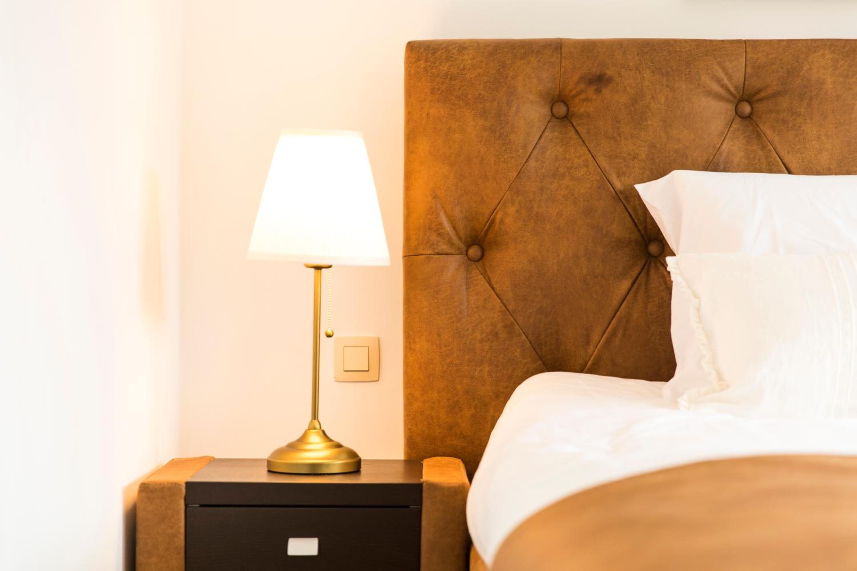 A neatly made bed with white linens, a tufted headboard, and a bedside table with a lamp.