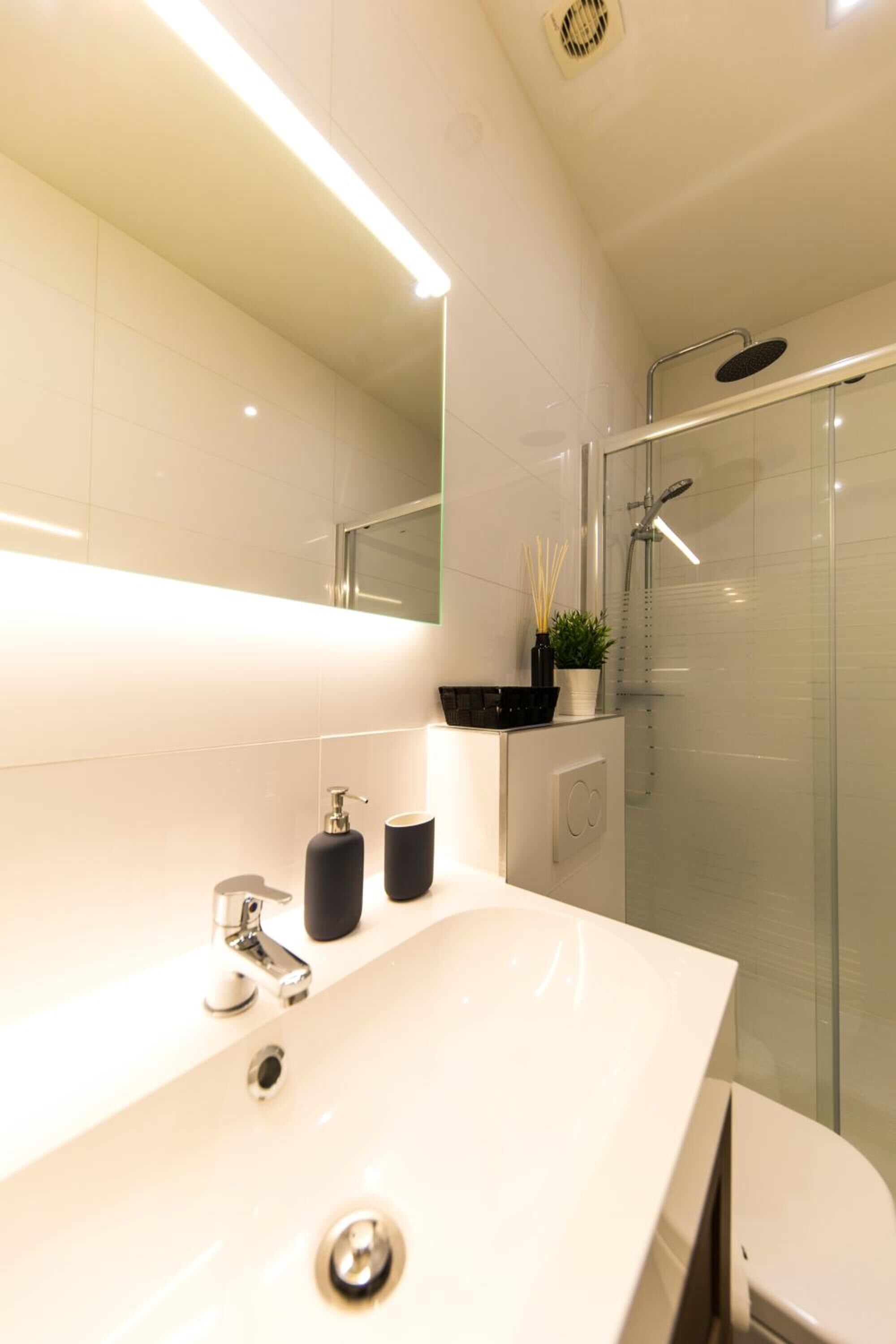 Une salle de bain moderne avec un grand miroir, un lavabo blanc et une douche à parois de verre.