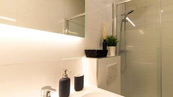 Une salle de bain moderne avec un grand miroir, un lavabo blanc et une douche à parois de verre.