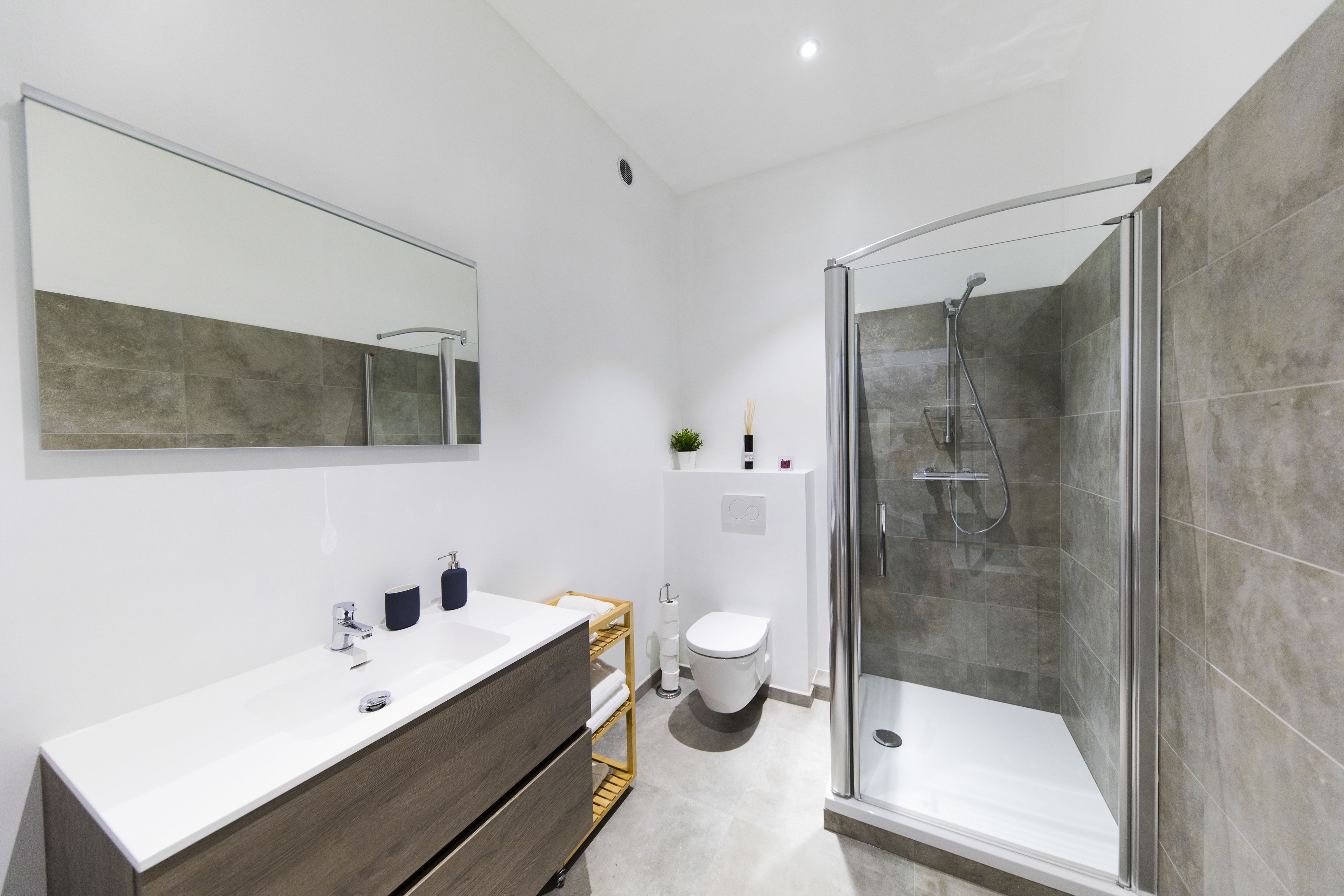 Une salle de bain moderne avec une douche à parois de verre, un meuble-lavabo en bois et un grand miroir.