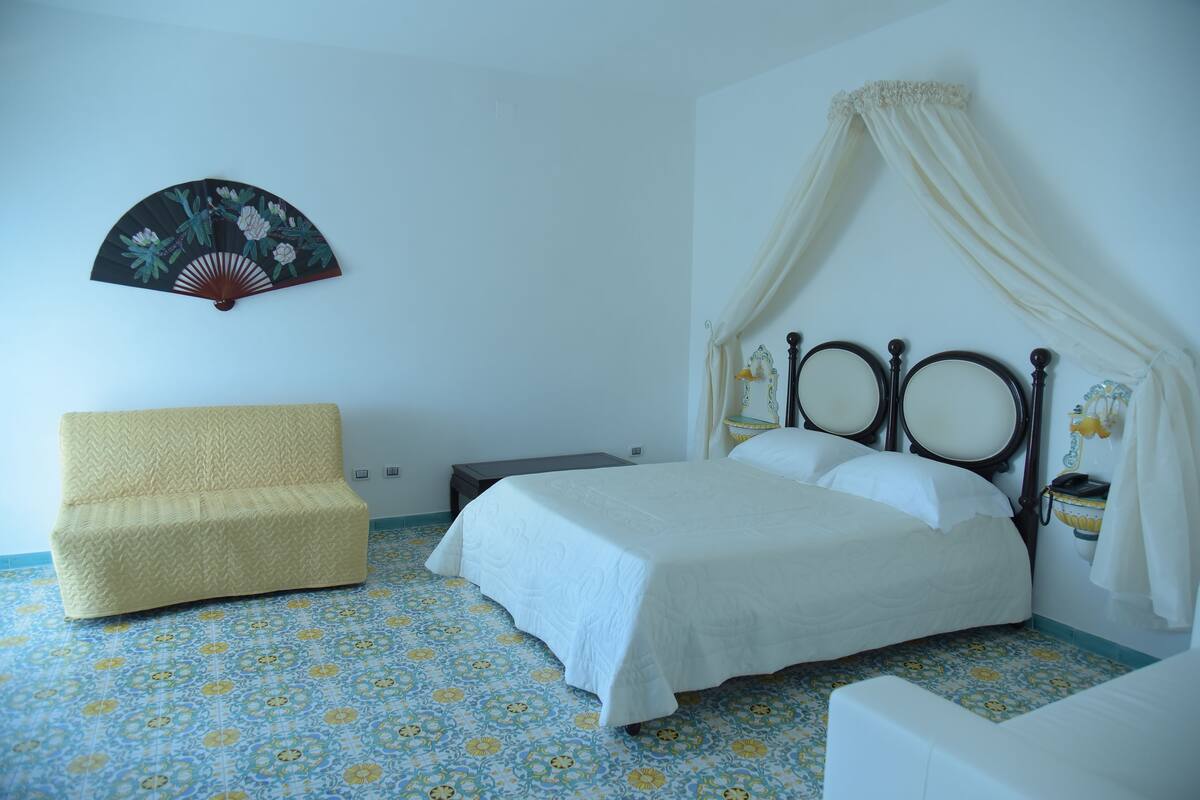 Ein Schlafzimmer mit einem Bett, einem Sessel, einem Nachttisch und einem Wandventilator.