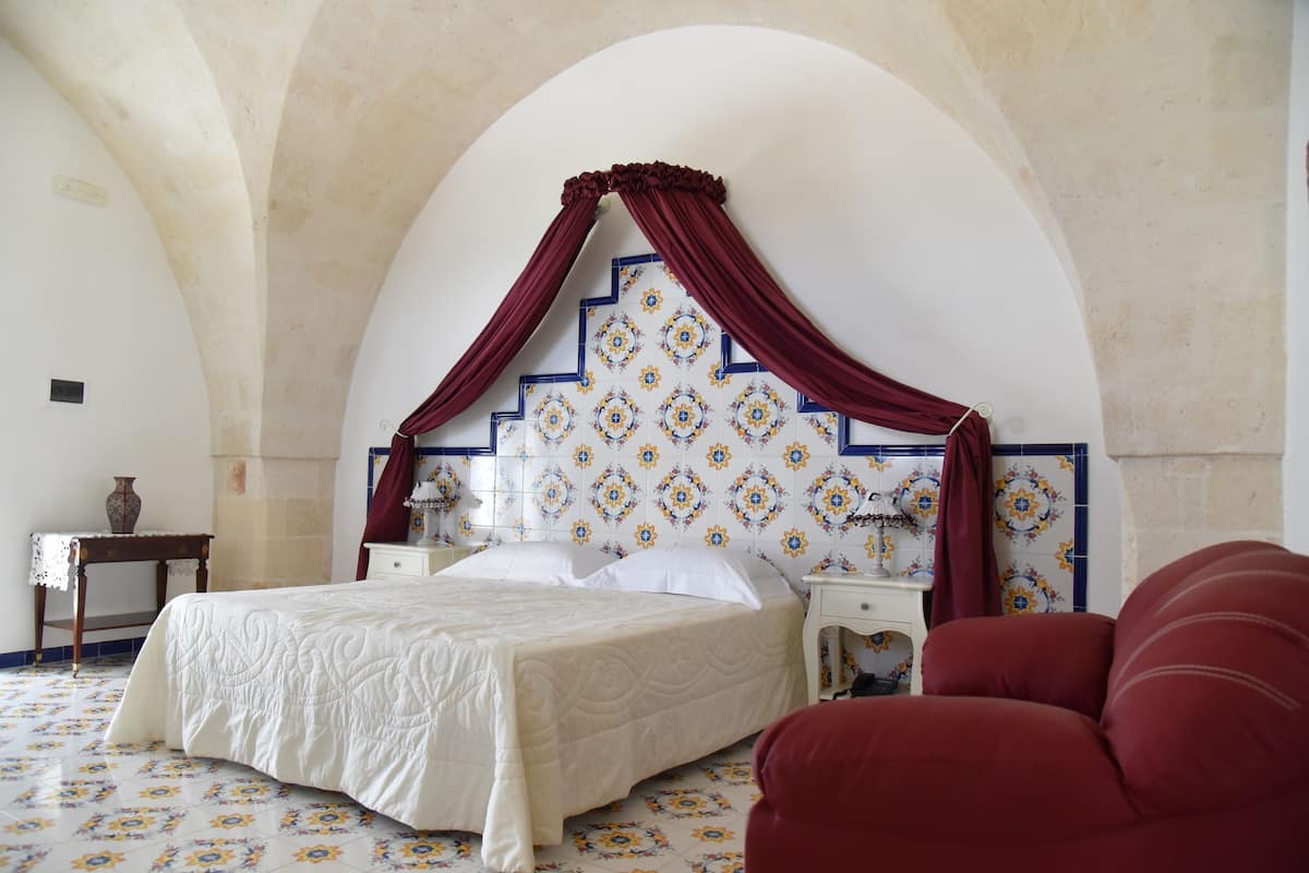 Ein Schlafzimmer mit einem großen Bett, einem Nachttisch, einem roten Sessel und einem dekorativen Kopfteil.