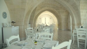 Un espace repas avec des tables et des chaises blanches, des arches en pierre et un sol carrelé.