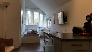A compact hotel room with a bed, a desk, a chair, and a kitchenette. - Apartmenthaus Somborn (Bochum)
