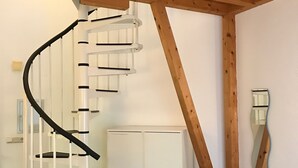 A spiral staircase with white steps and black handrails, a white wardrobe, and a black leather sofa in a room with wooden beams on the ceiling. - Apartmenthaus Somborn (Bochum)