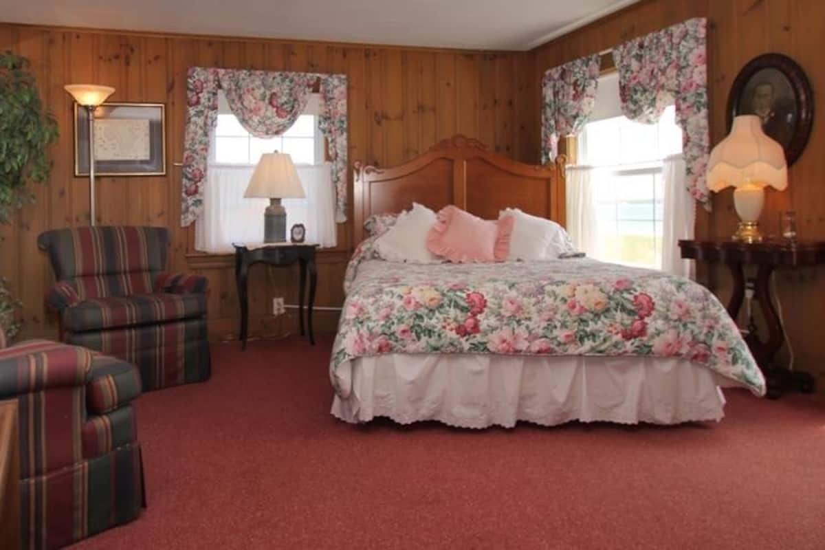 A cozy bedroom with a floral bedspread, a wooden headboard, and plaid chairs.