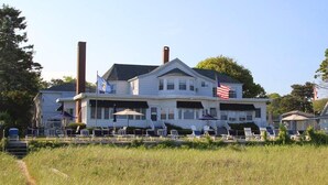 A large white building with multiple windows and a flagpole, surrounded by a grassy area with chairs and umbrellas. - Holiday House Inn (Scarborough)