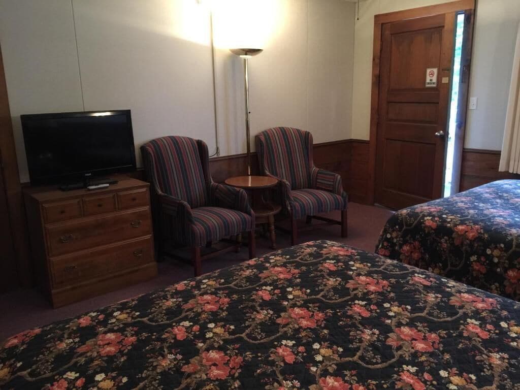 A hotel room with a TV, two striped armchairs, a small table, and floral bedspreads.