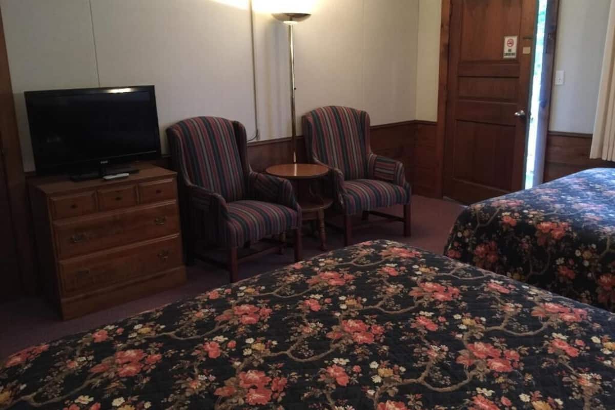 A hotel room with a TV, two striped armchairs, a small table, and floral bedspreads.