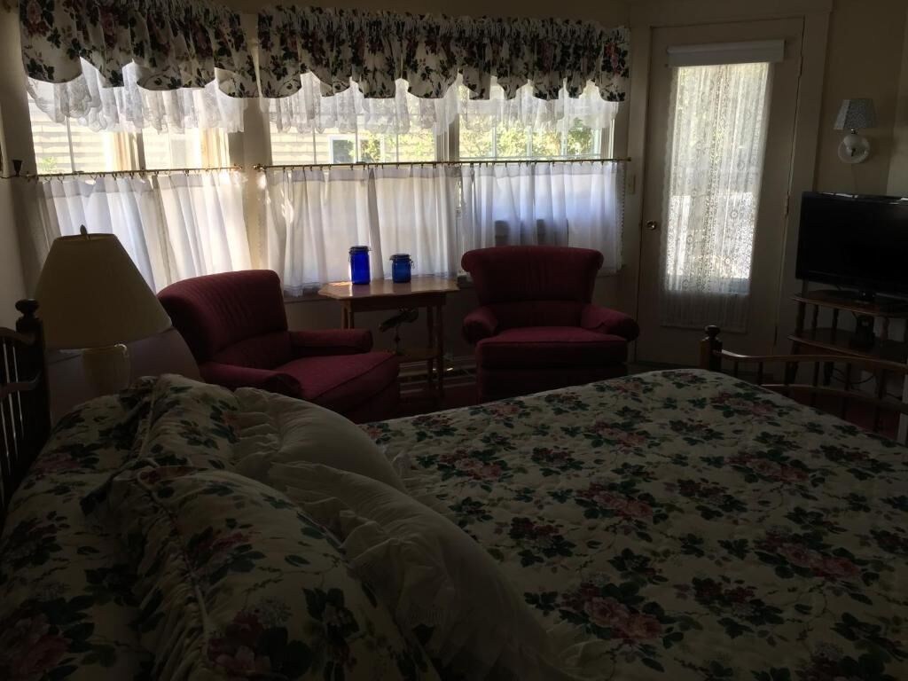 A bedroom with a bed, two chairs, a table, a lamp, and a television.