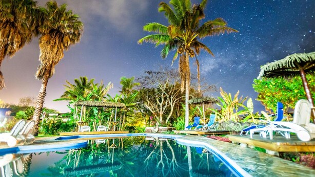 En swimmingpool med liggestole og palmer under en stjerneklar nattehimmel.