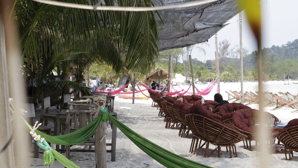 A beachside seating area with wicker chairs and a hammock under a shaded area, with a thatched hut in the background. - Sandbank Restaurant & Camping Koh Rong (Koh Rong)