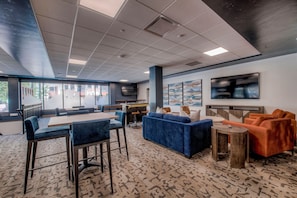 Relax in a stylish lounge area with sofas, a coffee table, and bar stools, surrounded by large windows offering views of the outdoors.