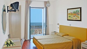 Habitación de hotel con cama, escritorio, silla, televisor, un cuadro y vista a la playa.