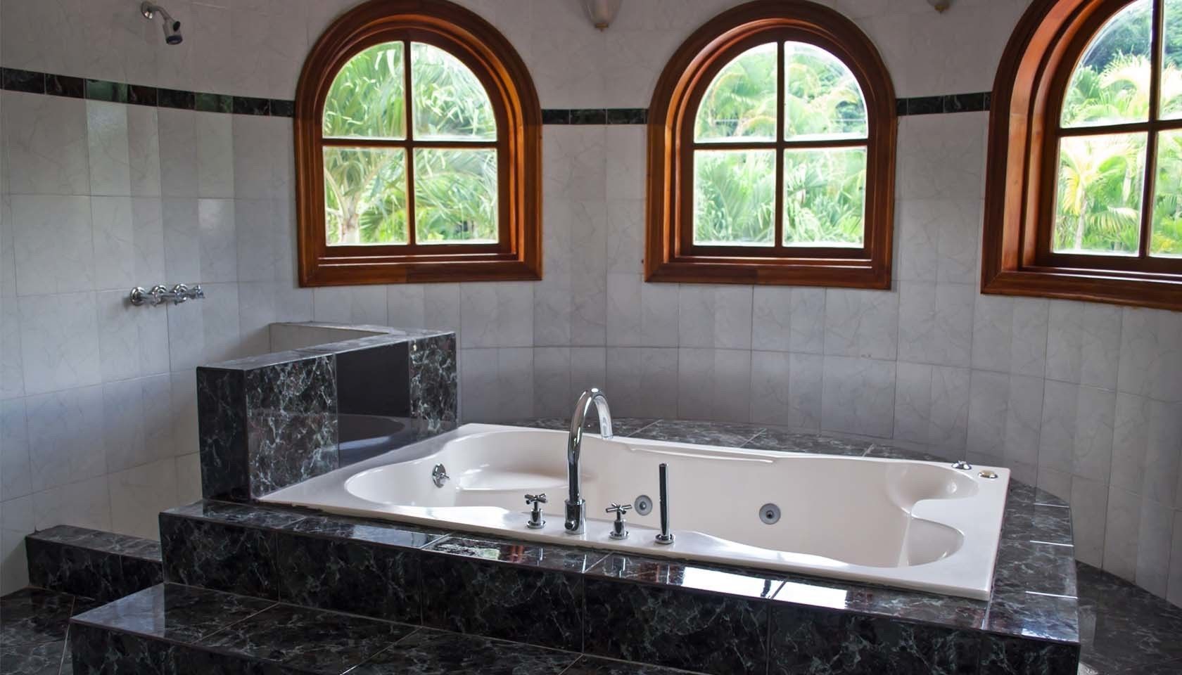 A modern bathroom with a freestanding bathtub, marble countertops, and arched windows with a view of greenery.