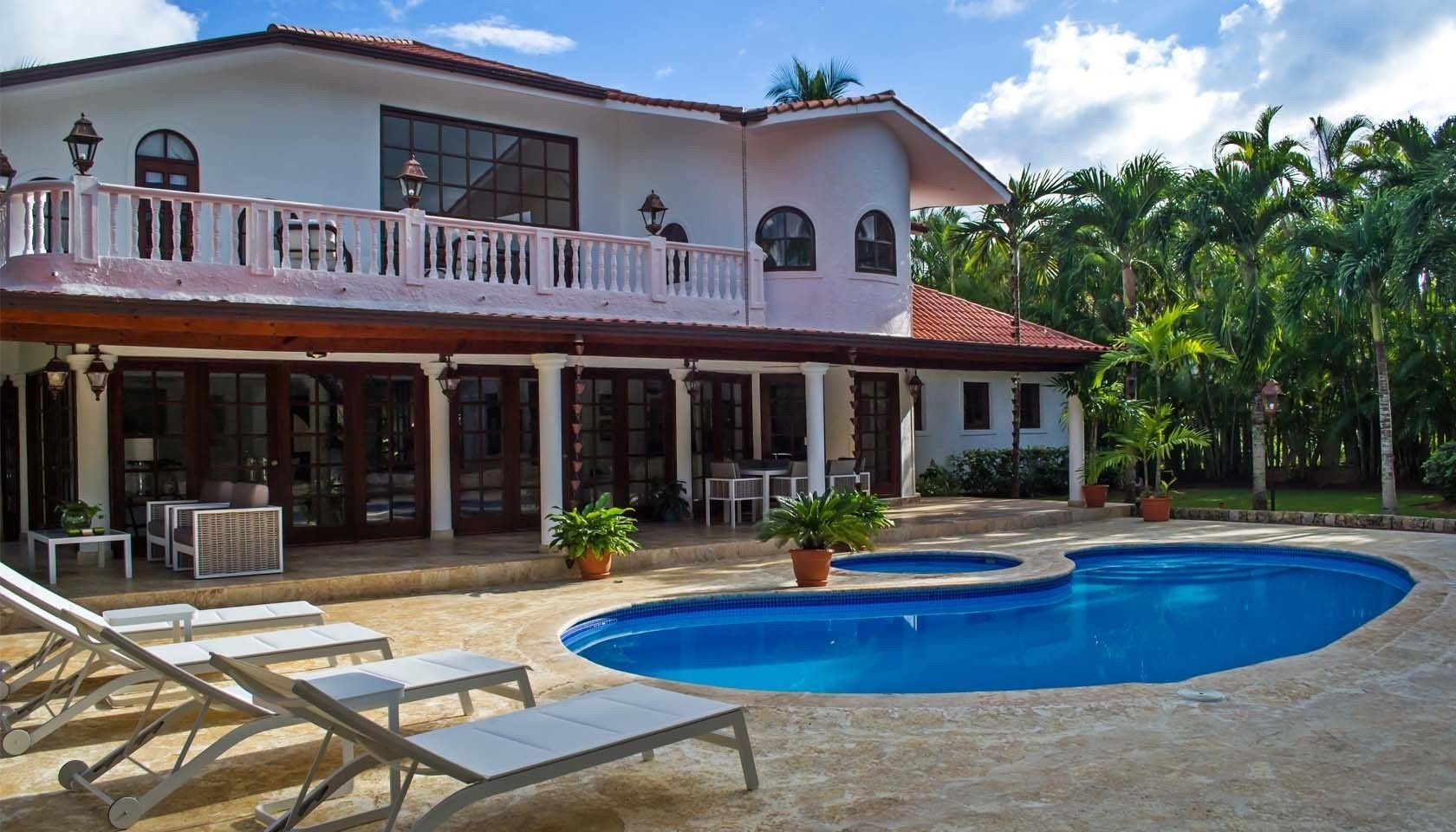 A two-story house with a swimming pool, outdoor furniture, and potted plants.