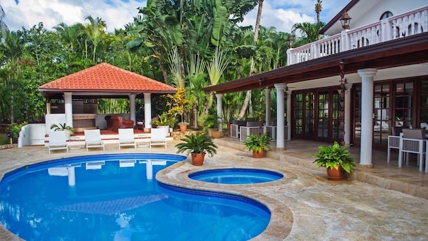 A pool area with two swimming pools, lounge chairs, and a covered seating area with a red roof. - Villa Alondra by Casa de Campo Resort & Villas (La Romana)