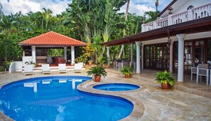 Uma área de piscina com duas piscinas, espreguiçadeiras e um espaço de estar coberto com telhado vermelho.