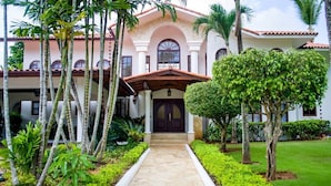 A two-story building with a central entrance, surrounded by a well-maintained garden with various plants and trees. - Villa Alondra by Casa de Campo Resort & Villas (La Romana)