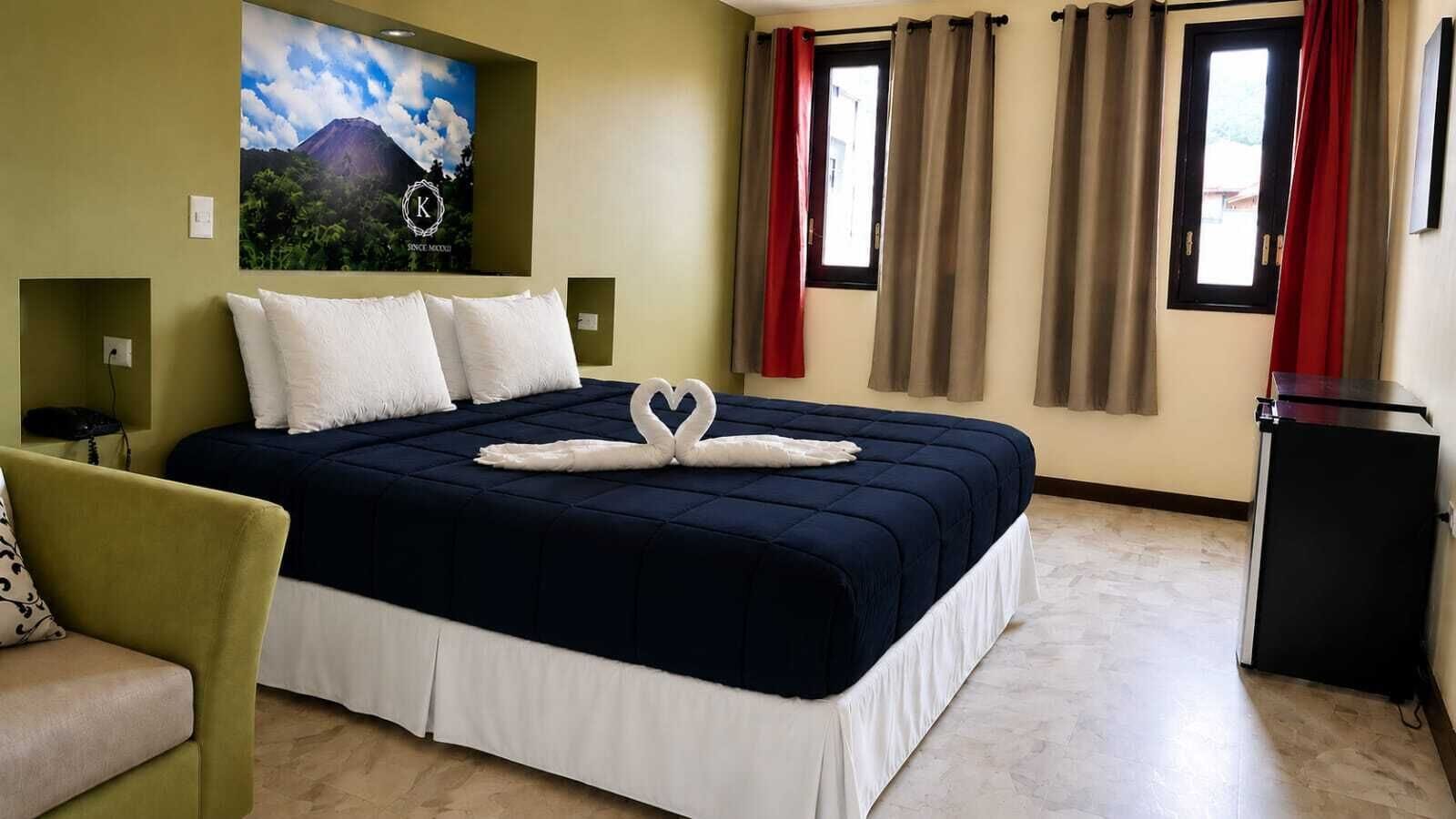 A hotel room with a bed, a desk, a chair, a refrigerator, and a wall-mounted TV.