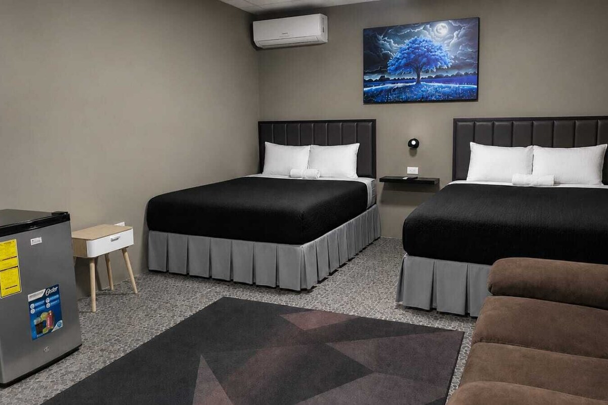 Ein Hotelzimmer mit zwei Betten, einem Kühlschrank, einem kleinen Tisch, einer Couch und einem Bild an der Wand.