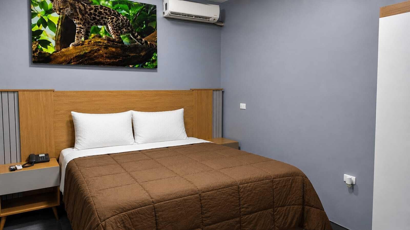 A hotel room with a bed, a nightstand, a telephone, and an air conditioning unit.
