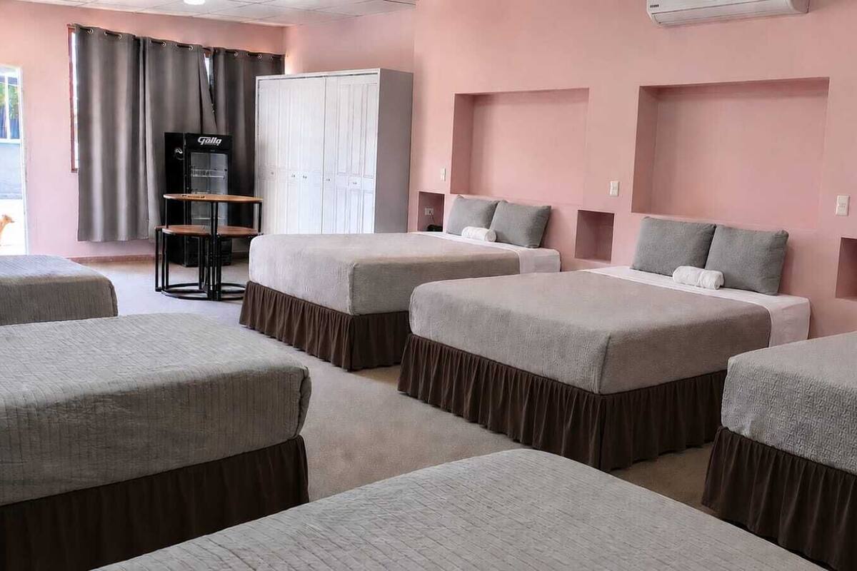 Una habitación de hotel con cuatro camas, un armario, un escritorio y un aire acondicionado.